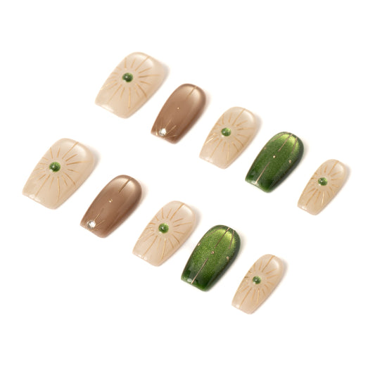 Flat lay of ten press-on nails arranged in two neat rows on a white background, featuring a neutral palette of cream, taupe, and deep green. The designs include subtle gold sunburst line art and small green gemstone accents, with a mix of glossy solid and softly shimmering finishes.