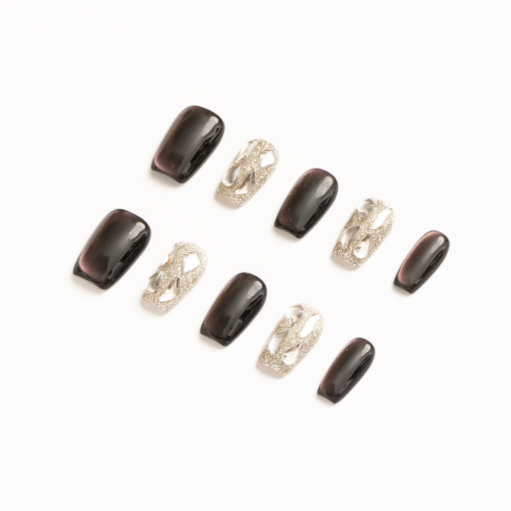 Flat lay of ten press-on nails arranged in two rows on a white background, featuring a dark plum and silver color palette. The set includes glossy deep purple cat-eye nails with subtle magnetic shimmer, paired with high-shine silver glitter accent nails adorned with sculptural metallic chain-style embellishments for a bold, modern luxe look.