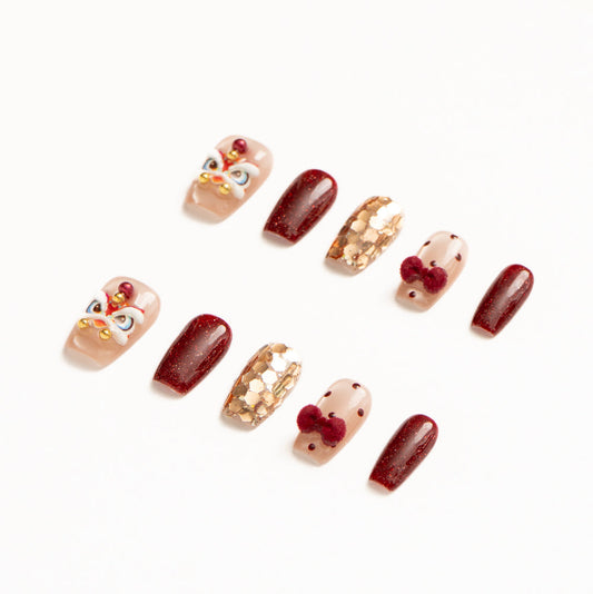 Flat lay of ten press-on nails arranged in two rows on a white background, featuring a festive red, gold, and nude color palette. The set includes glossy deep red shimmer nails, sheer nude accents with red polka dots and plush velvet bow details, gold foil mosaic textures, and statement nails with intricate mask-inspired designs accented by pearls and metallic beads for a bold, celebratory look. Lunar New Year nails