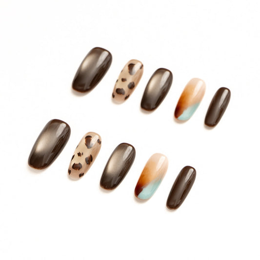 Flat lay of ten press-on nails arranged in two rows on a white background, featuring an earthy brown and neutral color palette. The set includes glossy chocolate-brown nails, metallic bronze cat-eye finishes, a sheer nude accent with leopard print spots, and a soft abstract ombré nail blending warm amber, cream, and muted teal for a modern, organic look.