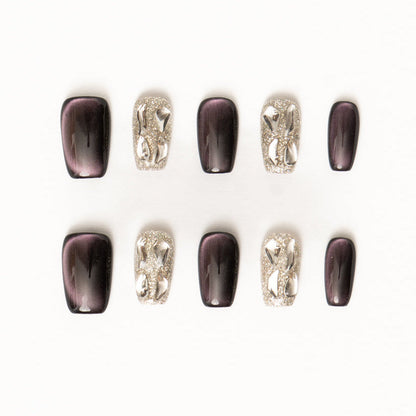 Flat lay of ten press-on nails arranged in two rows on a white background, featuring a dark plum and silver color palette. The set includes glossy deep purple cat-eye nails with subtle magnetic shimmer, paired with high-shine silver glitter accent nails adorned with sculptural metallic chain-style embellishments for a bold, modern luxe look.