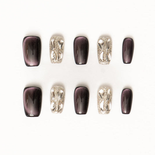 Flat lay of ten press-on nails arranged in two rows on a white background, featuring a dark plum and silver color palette. The set includes glossy deep purple cat-eye nails with subtle magnetic shimmer, paired with high-shine silver glitter accent nails adorned with sculptural metallic chain-style embellishments for a bold, modern luxe look.