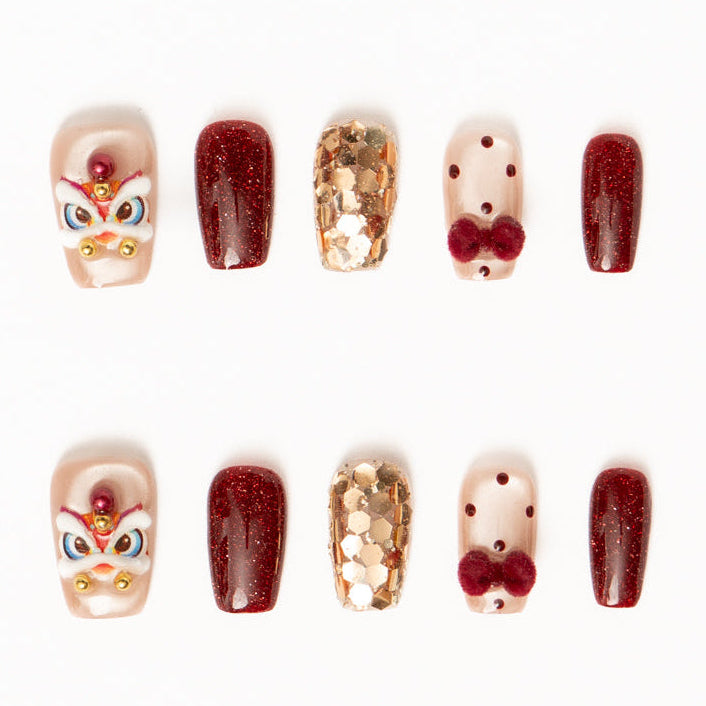 Flat lay of ten press-on nails arranged in two rows on a white background, featuring a festive red, gold, and nude color palette. The set includes glossy deep red shimmer nails, sheer nude accents with red polka dots and plush velvet bow details, gold foil mosaic textures, and statement nails with intricate mask-inspired designs accented by pearls and metallic beads for a bold, celebratory look. Lunar New Year nails