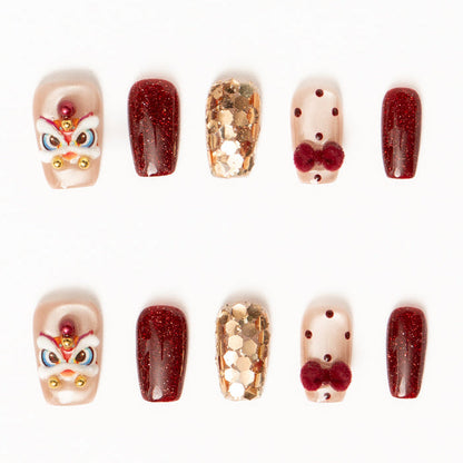 Flat lay of ten press-on nails arranged in two rows on a white background, featuring a festive red, gold, and nude color palette. The set includes glossy deep red shimmer nails, sheer nude accents with red polka dots and plush velvet bow details, gold foil mosaic textures, and statement nails with intricate mask-inspired designs accented by pearls and metallic beads for a bold, celebratory look. Lunar New Year nails