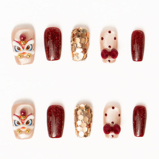 Flat lay of ten press-on nails arranged in two rows on a white background, featuring a festive red, gold, and nude color palette. The set includes glossy deep red shimmer nails, sheer nude accents with red polka dots and plush velvet bow details, gold foil mosaic textures, and statement nails with intricate mask-inspired designs accented by pearls and metallic beads for a bold, celebratory look. Lunar New Year nails