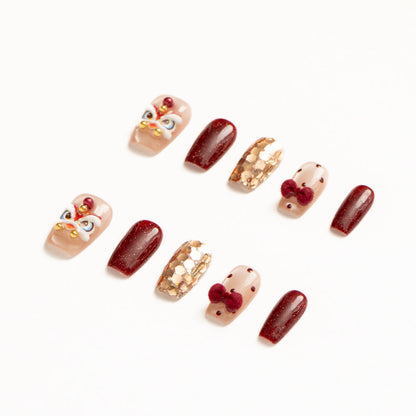 Flat lay of ten press-on nails arranged in two rows on a white background, featuring a festive red, gold, and nude color palette. The set includes glossy deep red shimmer nails, sheer nude accents with red polka dots and plush velvet bow details, gold foil mosaic textures, and statement nails with intricate mask-inspired designs accented by pearls and metallic beads for a bold, celebratory look. Lunar New Year nails