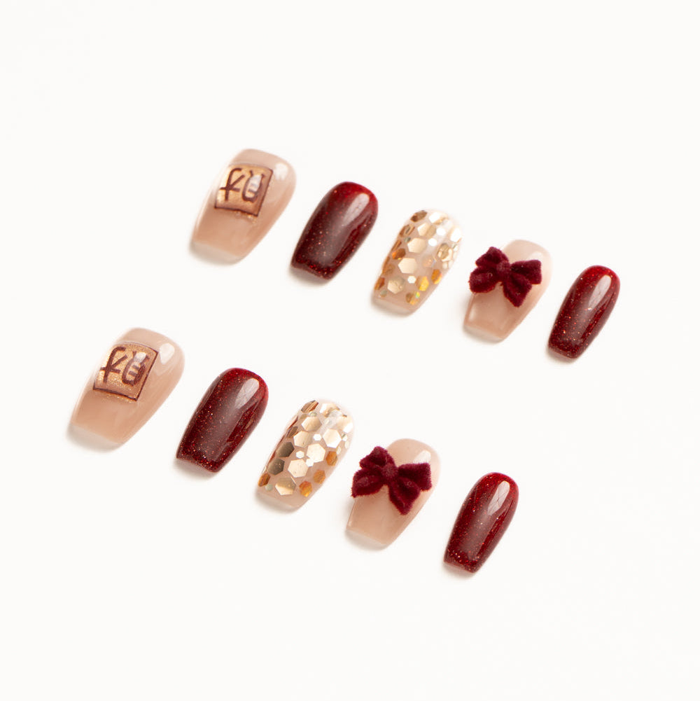 Flat lay of ten press-on nails arranged in two rows on a white background, featuring a deep burgundy and nude color palette. The set includes glossy wine-red shimmer nails, sheer nude accents with gold foil mosaic texture, plush velvet bow embellishments, and a minimalist nude nail with a small gold square charm for a luxe, lunarnewyear-inspired look.
