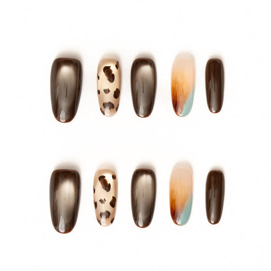 Flat lay of ten press-on nails arranged in two rows on a white background, featuring an earthy brown and neutral color palette. The set includes glossy chocolate-brown nails, metallic bronze cat-eye finishes, a sheer nude accent with leopard print spots, and a soft abstract ombré nail blending warm amber, cream, and muted teal for a modern, organic look.