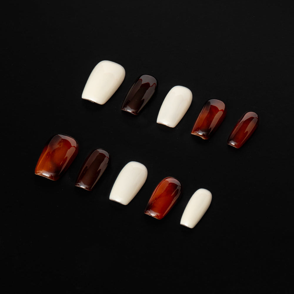 Flat lay of ten press-on nails arranged in two rows on a black background, featuring a minimal neutral color palette. The set alternates between glossy ivory white and deep espresso-brown nails with a translucent, glassy finish for a sleek, modern, and understated look.
