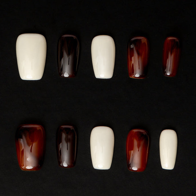 Flat lay of ten press-on nails arranged in two rows on a black background, featuring a minimal neutral color palette. The set alternates between glossy ivory white and deep espresso-brown nails with a translucent, glassy finish for a sleek, modern, and understated look.