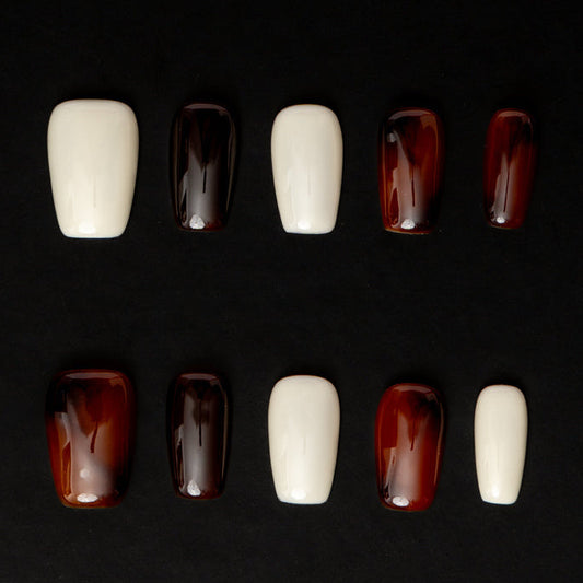 Flat lay of ten press-on nails arranged in two rows on a black background, featuring a minimal neutral color palette. The set alternates between glossy ivory white and deep espresso-brown nails with a translucent, glassy finish for a sleek, modern, and understated look.