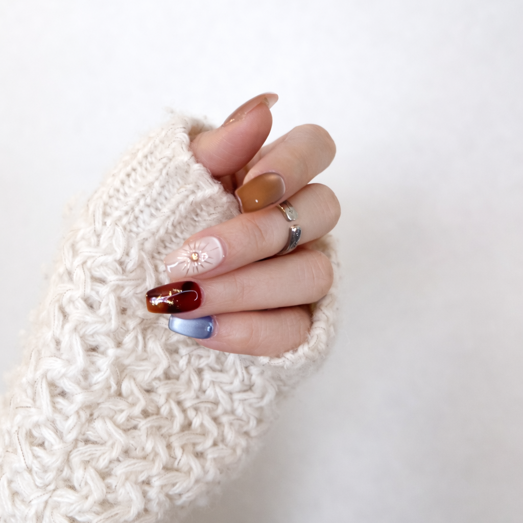 Woman wearing lumi loop Desert Solstice mix and match nails with a cozy white knit sweater, highlighting the amber and blue color palette.