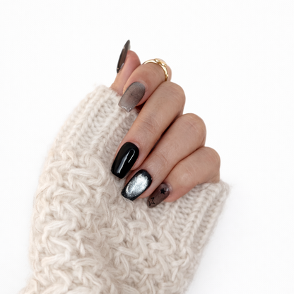 Woman wearing Midnight Star black and silver press-on nails with a cozy white knit sweater. Edgy Y2K manicure style.