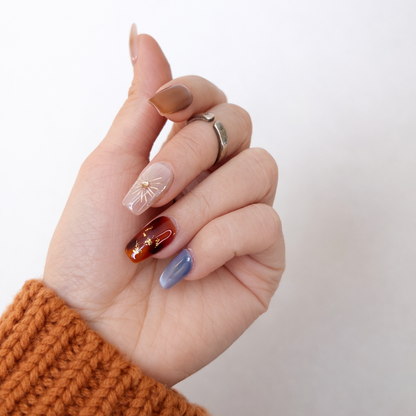 Hand model wearing boho style tortoise shell and gold sun press-on nails, styled with a rust orange knit sweater for a warm fall aesthetic.